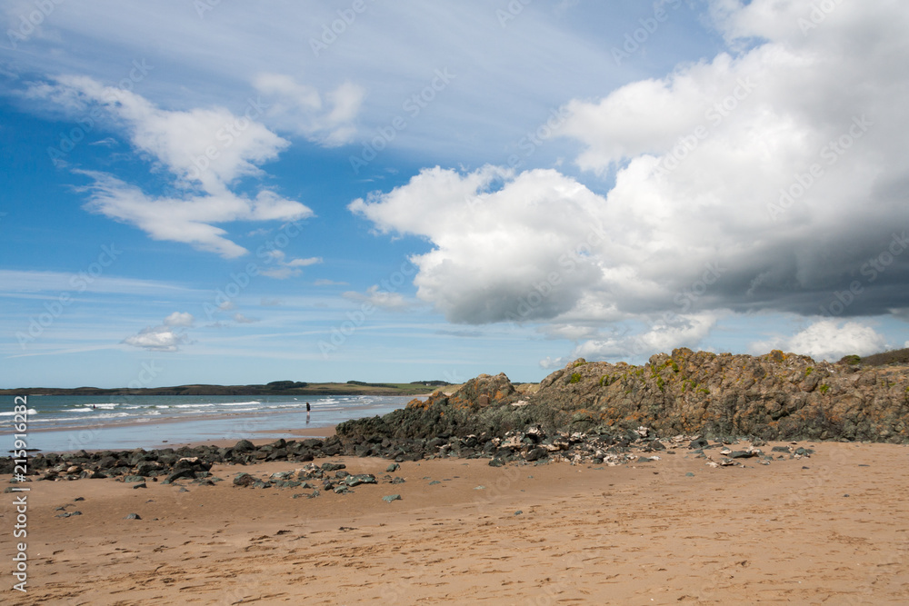 Volcanic rock, blue sky and clouds on Newborough beach, Anglesey, Gwynedd, Wales, United Kingdom