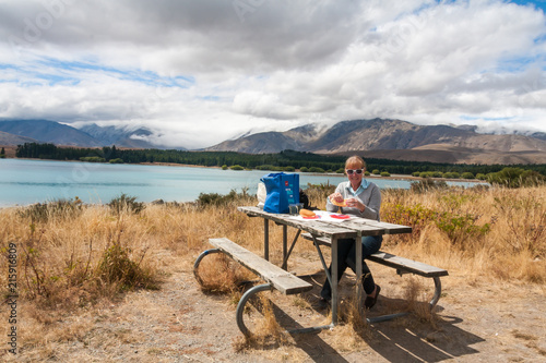 Senior woman eating at a picnic table by the shores of Lake Tekapo, South Island, New Zealand