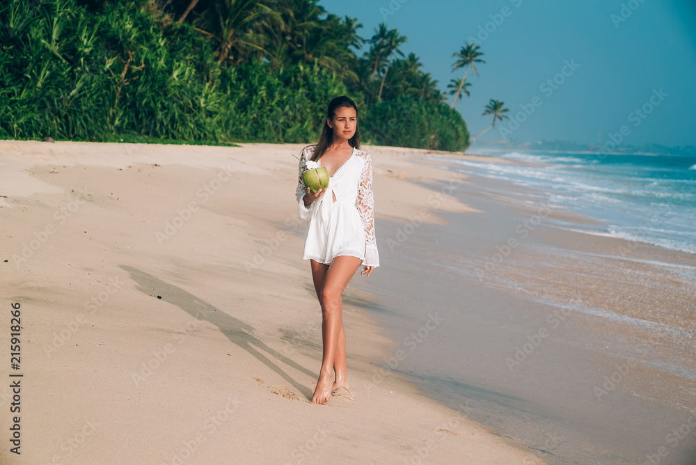 A beautiful brunette in white beach overalls walks along the seashore, admires the sandy white beach, wears stylish clothes. The concept of leisure, travel, people. A beautiful brunette in white beach overalls walks along the seashore, admires the sandy white beach, wears stylish clothes. The concept of leisure, travel, people.
