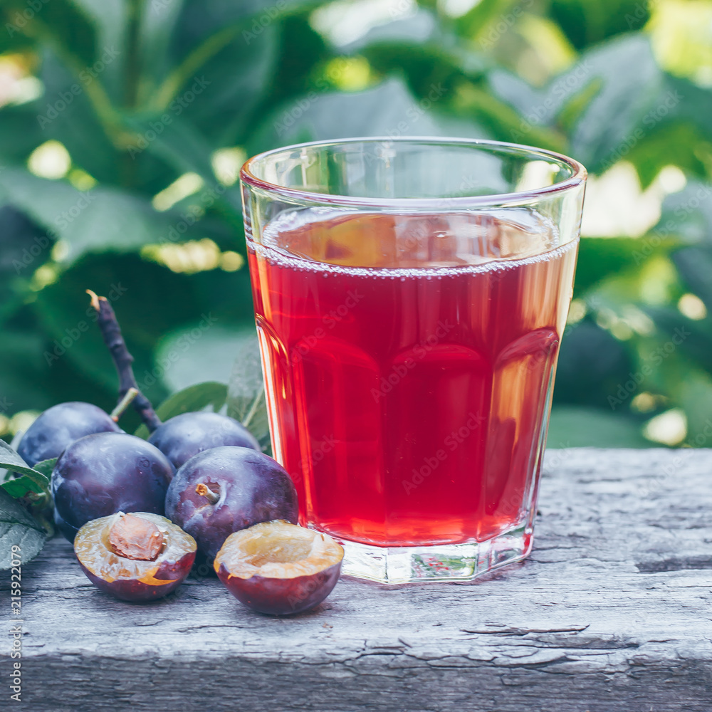 Plum juice in glass on wooden table background. Natural Green Leaf Background. Copy space. Toned image Plum juice in glass on wooden table background. Natural Green Leaf Background. Copy space. Toned image