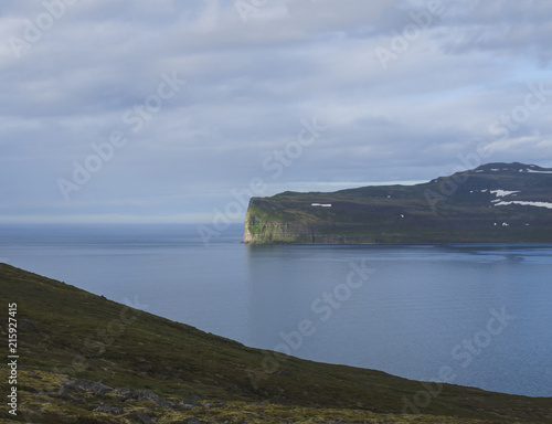 Scenic view from ocean on beautiful snow patched cliffs in west fjords, nature reserve Hornstrandir in Iceland, blue sea and cloudy sky background, golden hour light photo