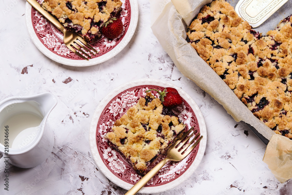 Honeysuckle crumble cake in a baking form and pieces of the cake on vintage plates on cracked concrete background. Homemade streusel berries pie. Breakfast Honeysuckle crumble cake in a baking form and pieces of the cake on vintage plates on cracked concrete background. Homemade streusel berries pie. Breakfast