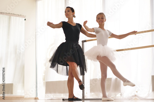 A teacher of classical dance teaches some steps to his young student who wants to learn how to dance and in the background the other little girls who listen. Concept of: ambition, education, teaching 