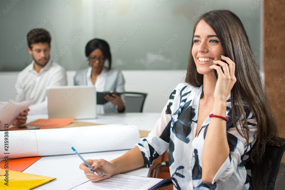 Smiling happy businesswoman talking on phone and making notes at her workplace in the office Smiling happy businesswoman talking on phone and making notes at her workplace in the office