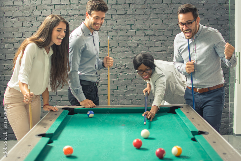 Fototapeta premium Young cheerful businesspeople playing billiards at office after work. 