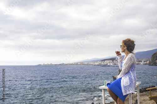 nice lady sitting on a desktop in front of the ocean drinking wine. alternative office and work location for digital nomad and modern people  photo