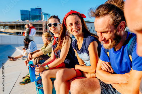 Group of hipster people travelers laughing and tell jokes while relaxing and sitting in summer sunset time in the city. Friendship, leisure, summer, gesture and people concept. © Iryna