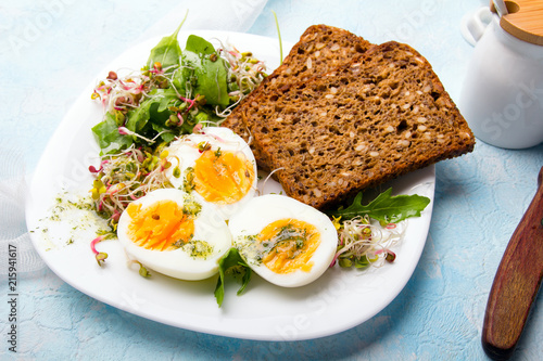 Zdrowe śniadanie: Jajka gotowane na twardo, świeże kiełki, rukola i kromka pełnoziarnistego chleba  na niebieskim tle, miejsce na tekst. 