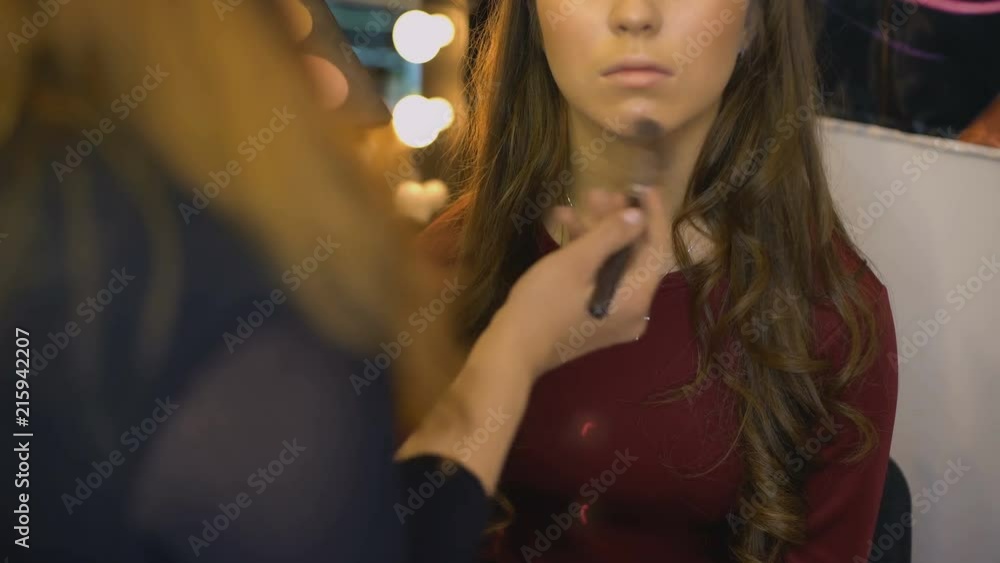 Make-up artist applying highlighter on model face, preparation for photo shoot Make-up artist applying highlighter on model face, preparation for photo shoot