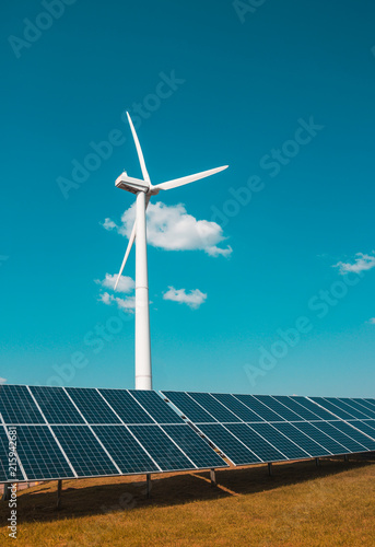 wind generator of electricity from three blades and solar panels of a battery of photocells against a background of clouds and a blue sky orange grass