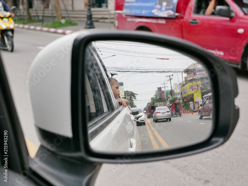 Reflection, in a car's wing mirror, of Asian baby girl enjoying sticking her head out and seeing view out side of the car