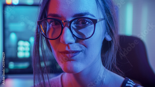 Portrait of the Beautiful Young Pro Gamer Girl Sitting at Her Personal Computer and Looks into Camera. Attractive Geek Girl Player Wearing Glasses in the Room Lit by Neon Lights. Stock Photo | Portrait of the Beautiful Young Pro Gamer Girl Sitting at Her Personal Computer and Looks into Camera. Attractive Geek Girl Player Wearing Glasses in the Room Lit by Neon Lights. Stock Photo |