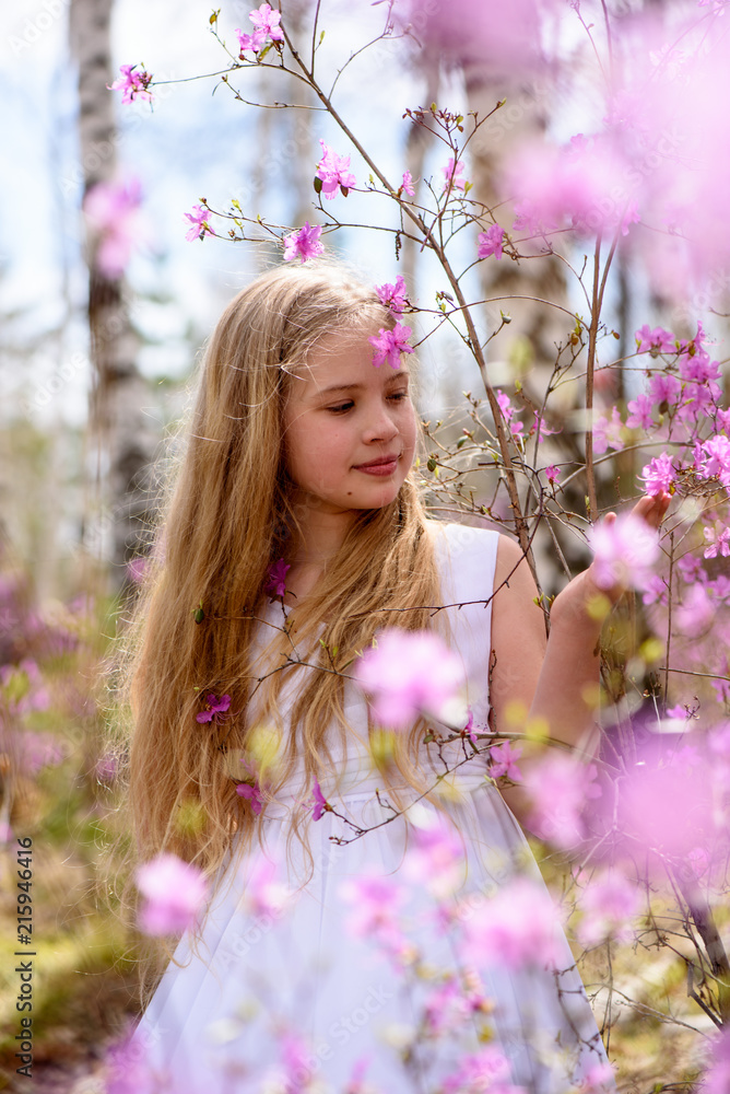 Fototapeta premium A child stands among the ledum and birch in white dress, smiling and fly hair