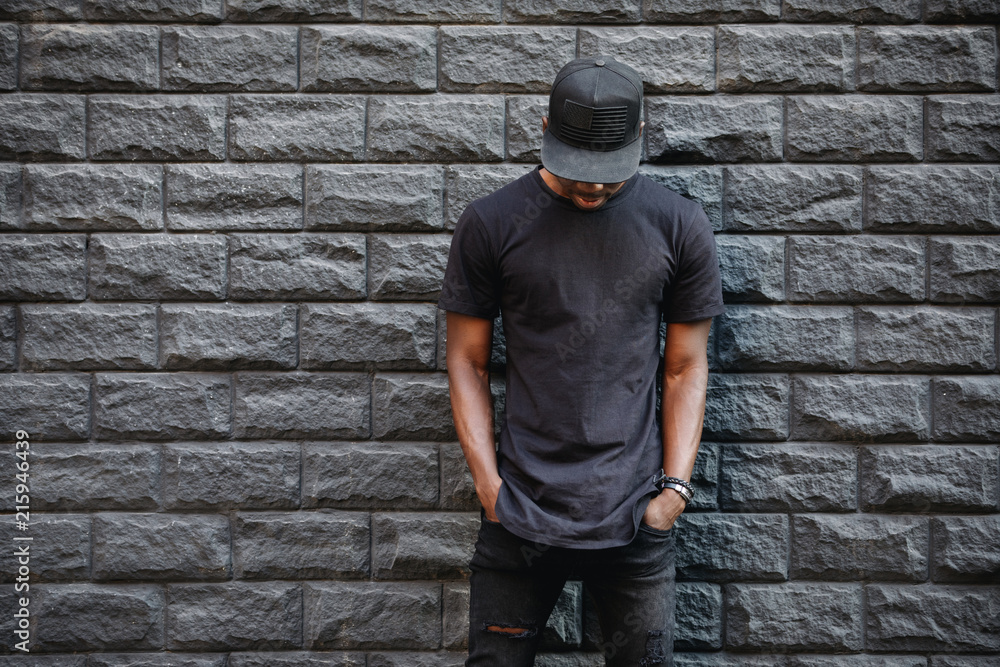 Handsome african american man in blank black t-shirt standing against brick wall - obrazy, fototapety, plakaty 