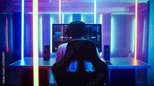 Back View Shot of the Beautiful Professional Gamer Girl Putting on Headset and Starts Playing Online Video Game on Her Personal Computer. Cute Casual Geek Girl. Lit by Neon Lamps in Retro Arcade Style