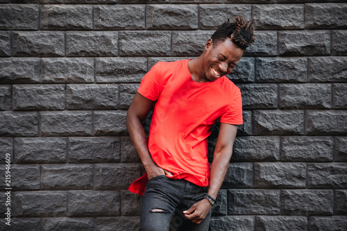 African male model in empty red t-shirt laughing against brick wall