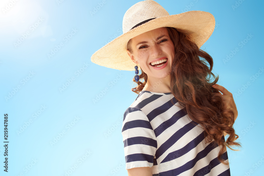 Portrait of smiling stylish woman in straw hat against blue sky