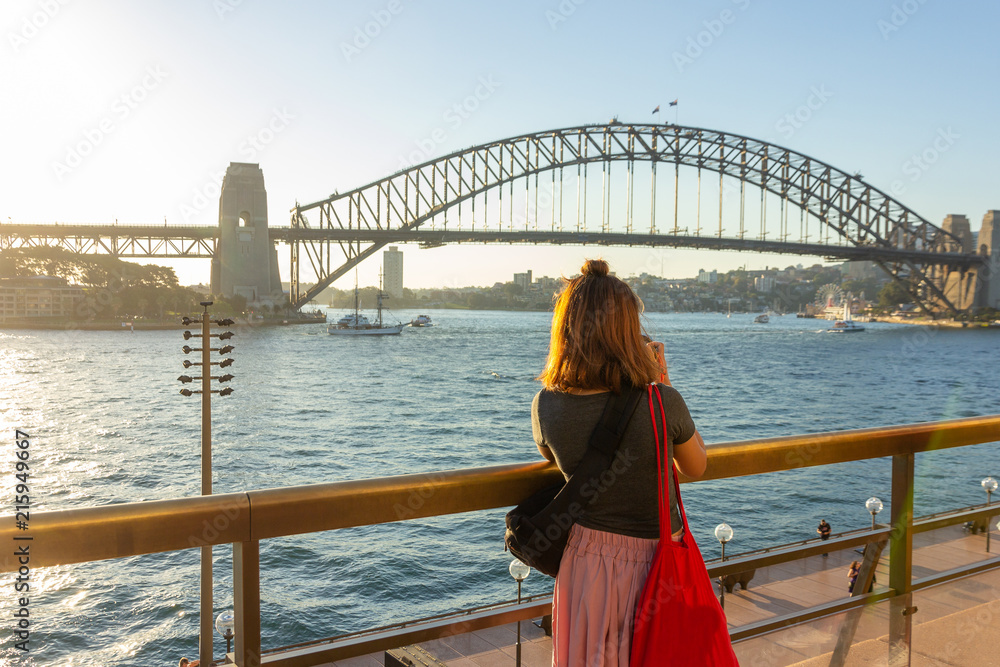 Naklejka premium Turystka z plecakiem robi zdjęcia Sydney Harbour Bridge podczas letniej wakacyjnej wycieczki.