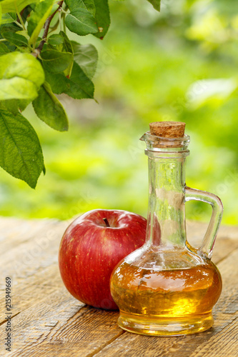 Apple vinegar in glass bottle and fresh red apple on wooden boar