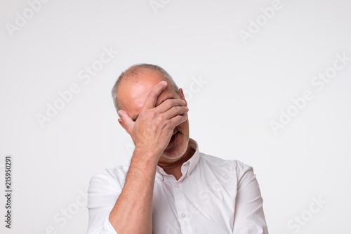 Displeased mature man in white shirt covering his eyes over gray background photo