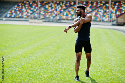African american male athlete in sportswear doing stretching exercise at stadium.