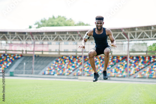 African american male athlete in sportswear doing jump exercise at stadium.