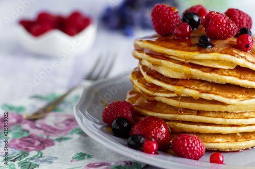 Stack of gold pancakes with berries and honey on wooden background
