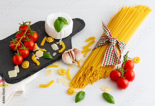 Bunch of uncooked long italian spaghetti tied with a cord in the colours of the national flag on white background. Served with cherry tomatoes,basil,chesse.Culinary background