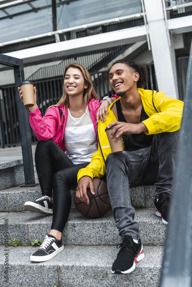 Obraz premium multiethnic couple with ball for basketball drinking coffee at city street