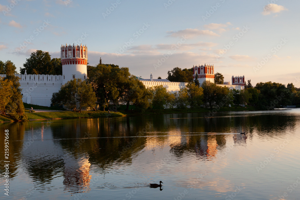 The walls and towers of the Novodevichy monastery in Moscow are reflected in the water in the summer evening sunset The walls and towers of the Novodevichy monastery in Moscow are reflected in the water in the summer evening sunset