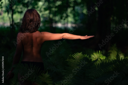 Pretty brunette woman walk in forest. Standing back with leaf tattoo on skin