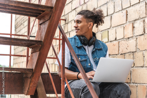 focused mixed race male freelancer in headphones working with laptop and looking away at street © LIGHTFIELD STUDIOS