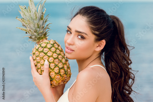 portrait of attractive young woman holding sweet pineapple near the sea