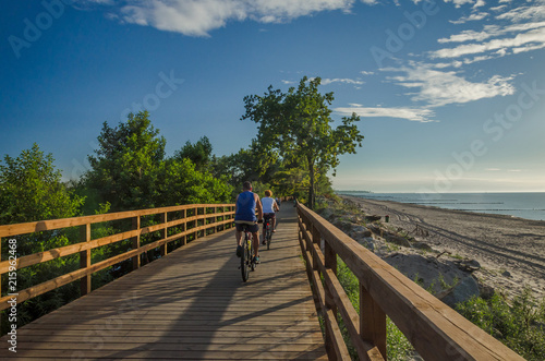Foto HOLIDAY SUNSET -  Holidaymakers on bike path by the sea shore