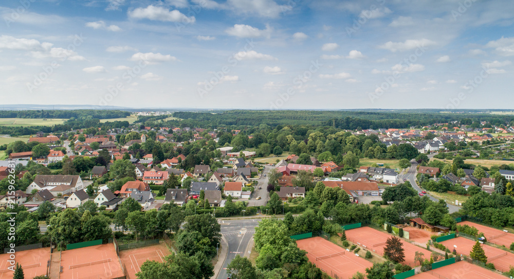Obraz premium Widok z lotu ptaka z przedmieścia niemieckiego miasta z szerokim widokiem po horyzont, kort tenisowy i domy jednorodzinne na przedmieściu.