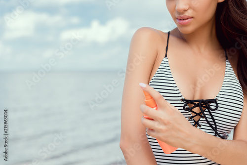 cropped view of young woman in swimsuit applying sunscreen on body
