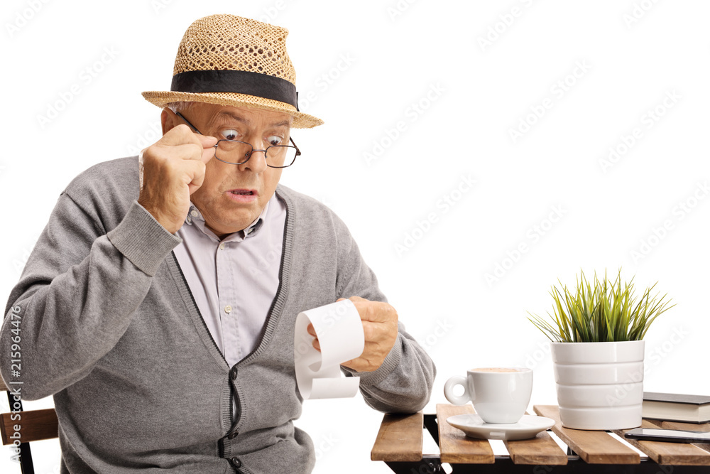 Shocked mature man seated at a coffee table looking at the bill Shocked mature man seated at a coffee table looking at the bill