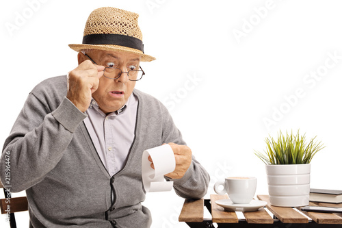 Shocked mature man seated at a coffee table looking at the bill photo