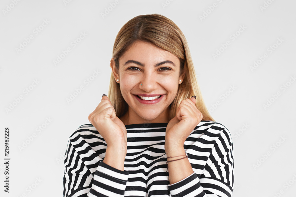 Picture of happy ecstatic young European female in stylish clothes clenching fists and smiling excitedly, overjoyed with great news, celebrating long awaited salary raise or promotion at work Picture of happy ecstatic young European female in stylish clothes clenching fists and smiling excitedly, overjoyed with great news, celebrating long awaited salary raise or promotion at work