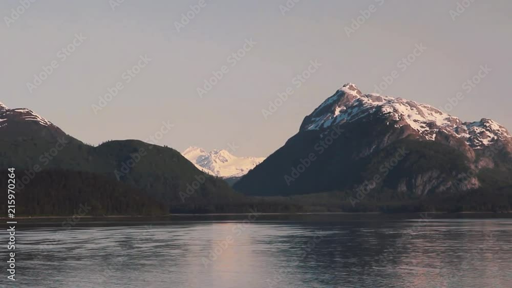 A view of the incredible undisturbed scenery of Glacier Bay, Alaska on a sunny day. Calm clear water with towering snow capped mountain peaks in the background. A view of the incredible undisturbed scenery of Glacier Bay, Alaska on a sunny day. Calm clear water with towering snow capped mountain peaks in the background.