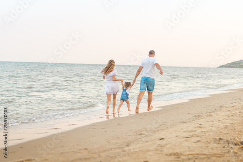 Close up Happy family of three - beatiful wife, father and daughter having fun walking on beach at sunset. Family traveling concept.