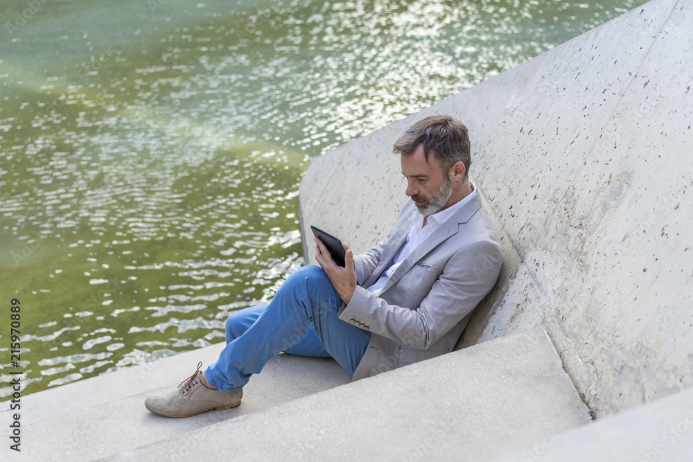 Businessman sitting on steps outdoors using tablet Businessman sitting on steps outdoors using tablet
