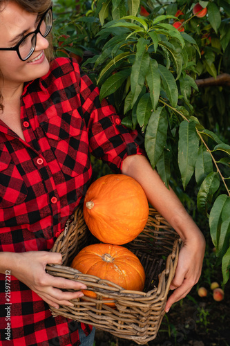 Woman is standing in the garden and holding orange pumpkins in her hands. Season harvesting. 