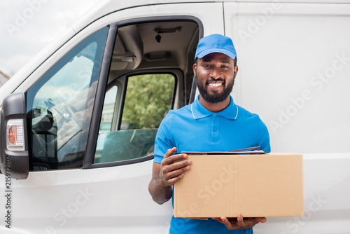 smiling african american delivery man holding cardboard box and looking at camera © LIGHTFIELD STUDIOS