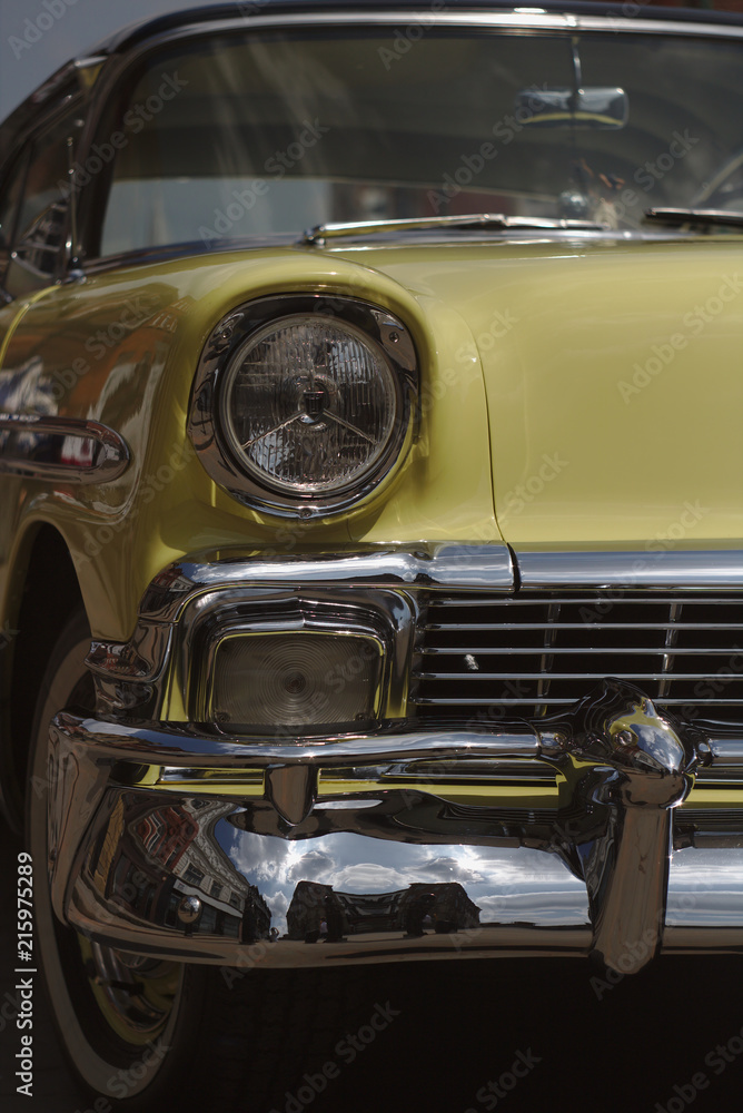 A close-up image of a classic1957 Chevrolet Bel-air with yellow paintwork and a black roof and shining chrome .