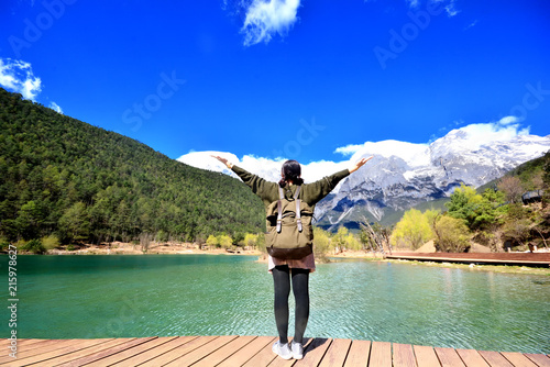 back of girl travel alone stand in front of extremely blue river ,Blue Moon valley, Jade Dragon Snow Mountain seen from a distance, Lijiang, China