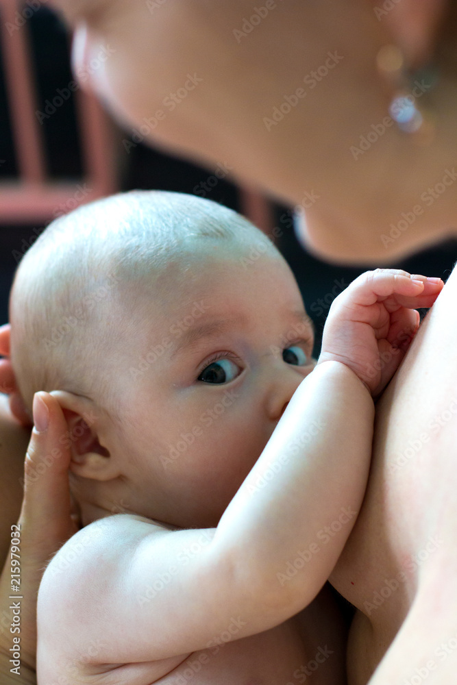 Newborn baby with cute expression is sucking mother's breast and