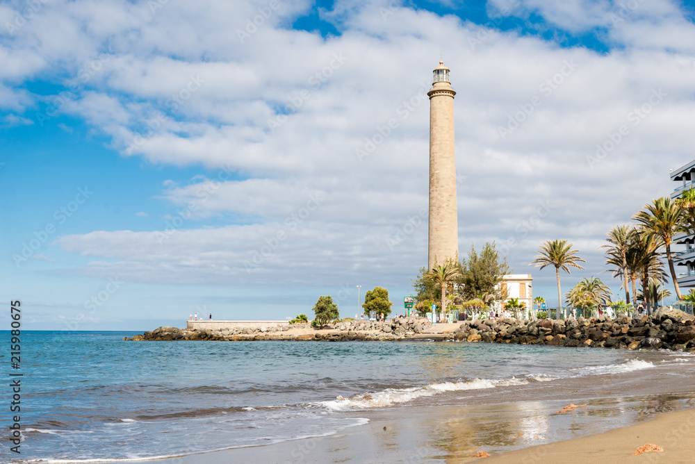 Tenerife, Canarias islands/ Spain - July 22, 2018: View of empty beach of tourists and high lighthouse on Canarias, view of bay with palms. Blue Atlantic ocean and beach on Gran Canaria.