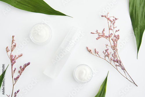 White cream bottle placed, Blank label package for mock up on a green foliage background and flowers. The concept of natural beauty products.