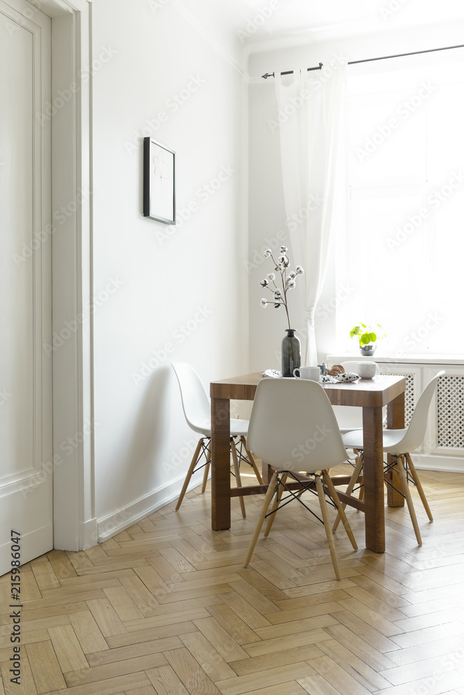 Wooden dining table with flowers in vase, two mugs and four chairs in real photo of bright room interior with window with drapes